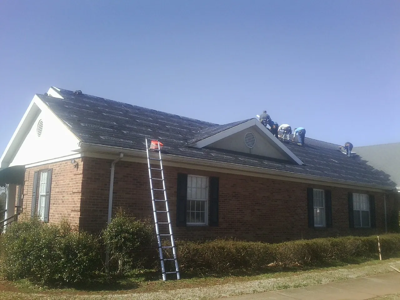 Crew tearing shingles off a brick ranch roof with a ladder set — Emergency Roof Repair work by our crew in Sabin