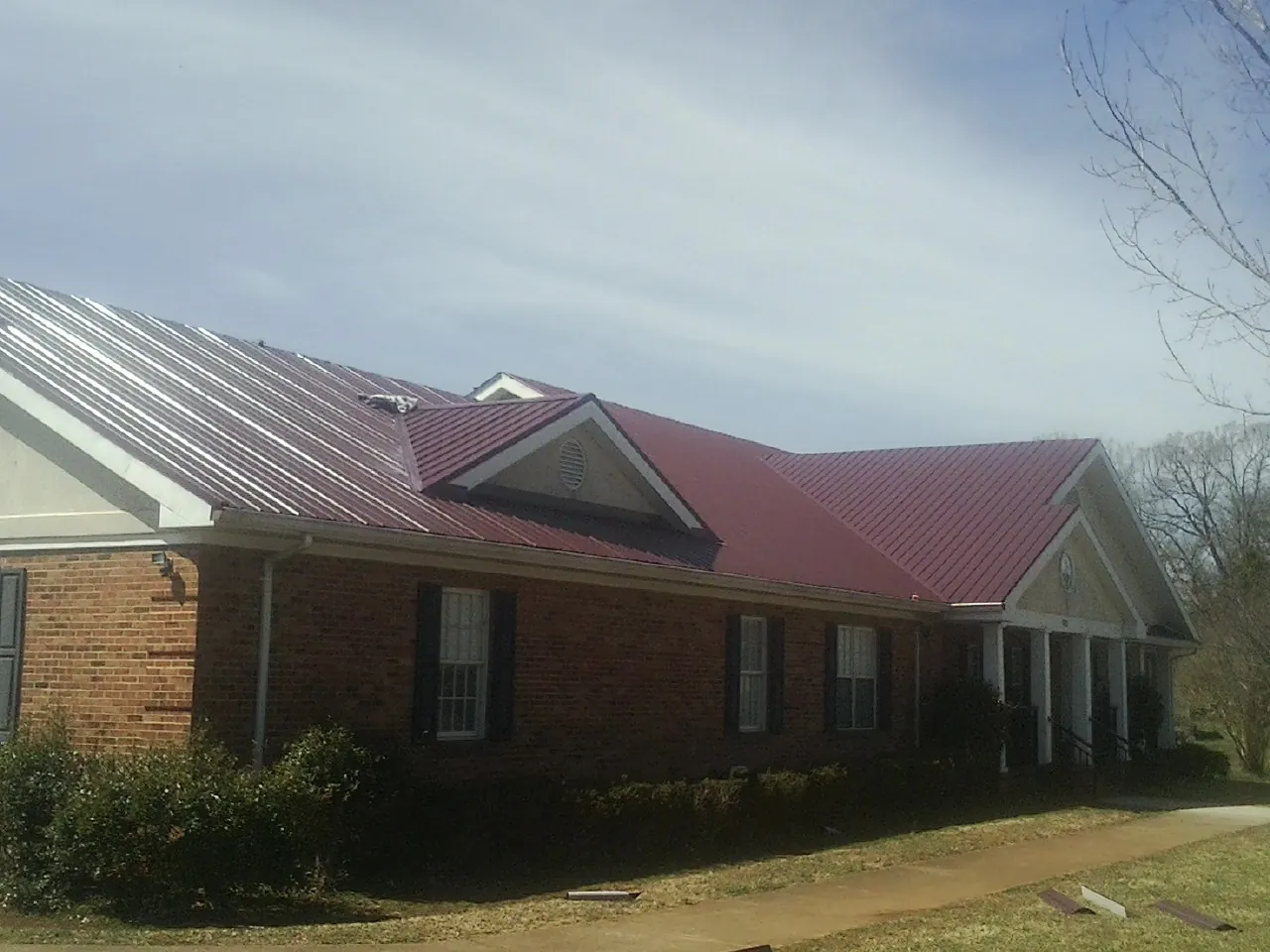 Red metal roof with gabled entries on a long brick building, from a Hail Damage Roof Repair job in Sabin