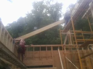 Carpenter raising a rafter beam on a new second story frame in Sabin