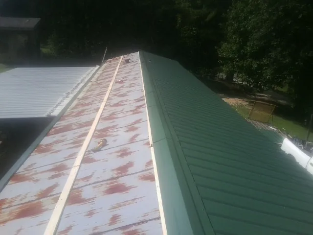 Old rusted panels beside newly installed green metal roofing — Wind Damage Roof Repair by Roofing Brothers in Sabin
