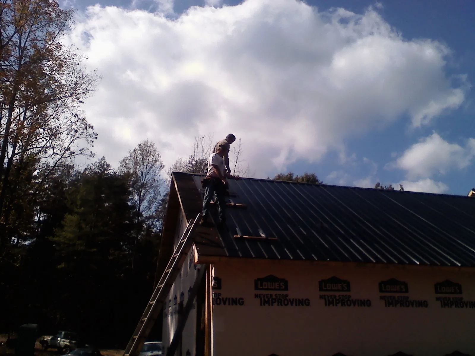 Roofer fastening dark metal panels high against a cloudy sky, from a Roof Inspection job in Sabin