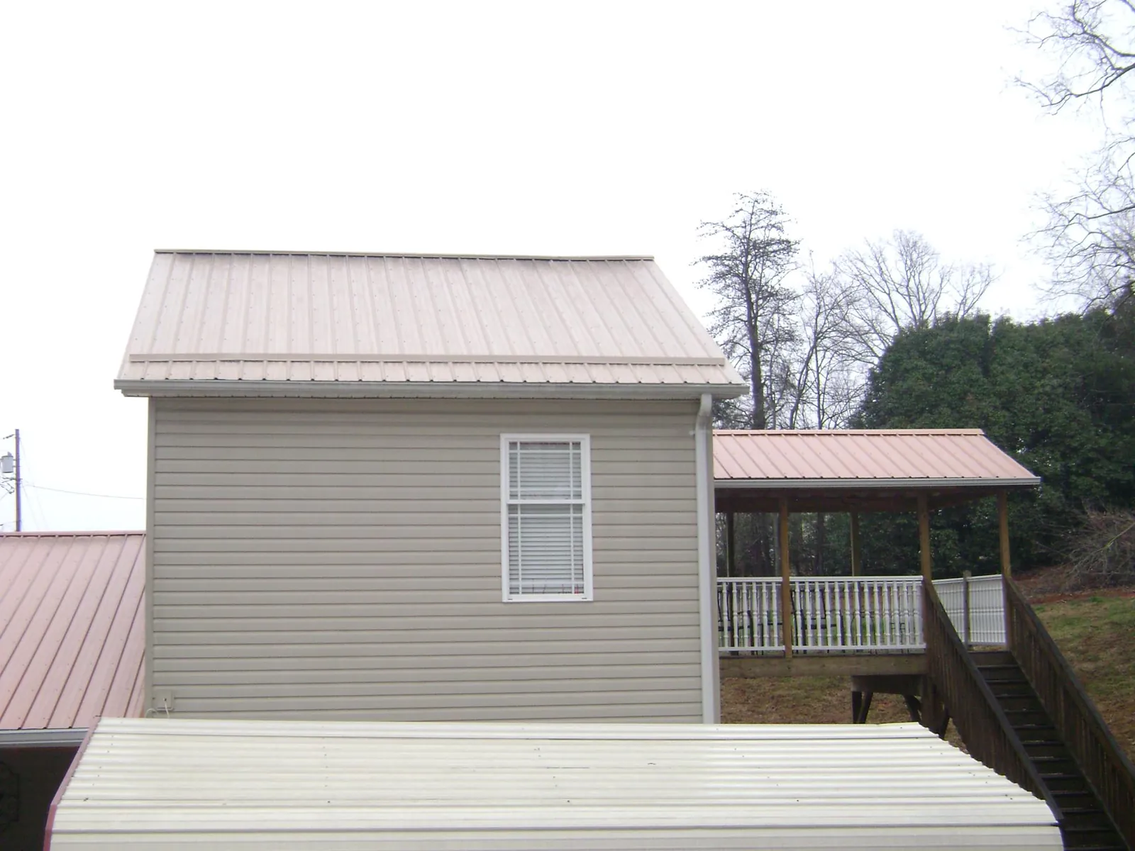 Tan metal roofs on a two story addition and attached porch, from a Roof Replacement job in Sabin